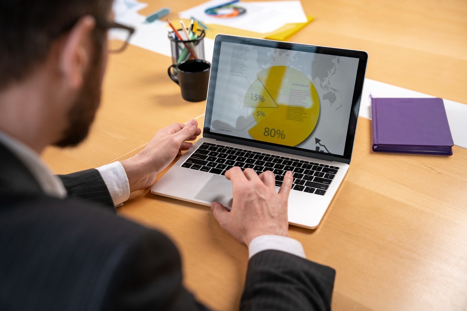 An over-the-shoulder view of a professional in a suit reviewing a yellow pie chart with percentage breakdowns on a laptop screen to optimize retargeting campaigns.